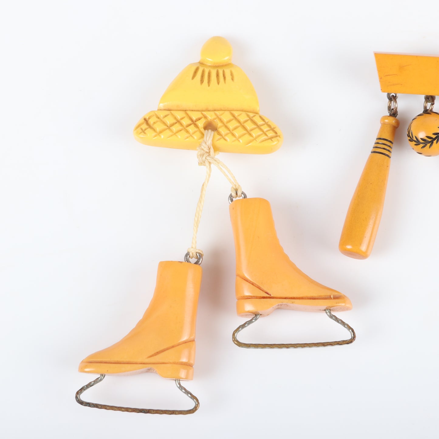 Vintage Bakelite 2pc. sports theme dangle charm pins. Carved butterscotch ice skates and cap, and baseball, bat and glove charms on bar pin. 4 1/4" H x 2 1/2" W (one)