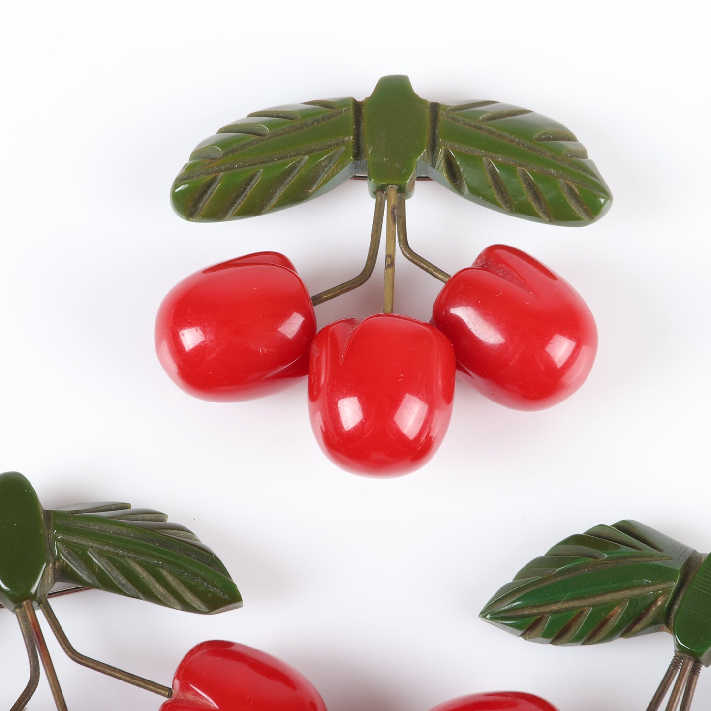 Vintage Bakelite set of 3 unusual cherry fruit pins. Each featuring 3 carved red cherries suspended with metal wire from carved green bakelite leaves. 2 1/4" H x 2 1/2" W