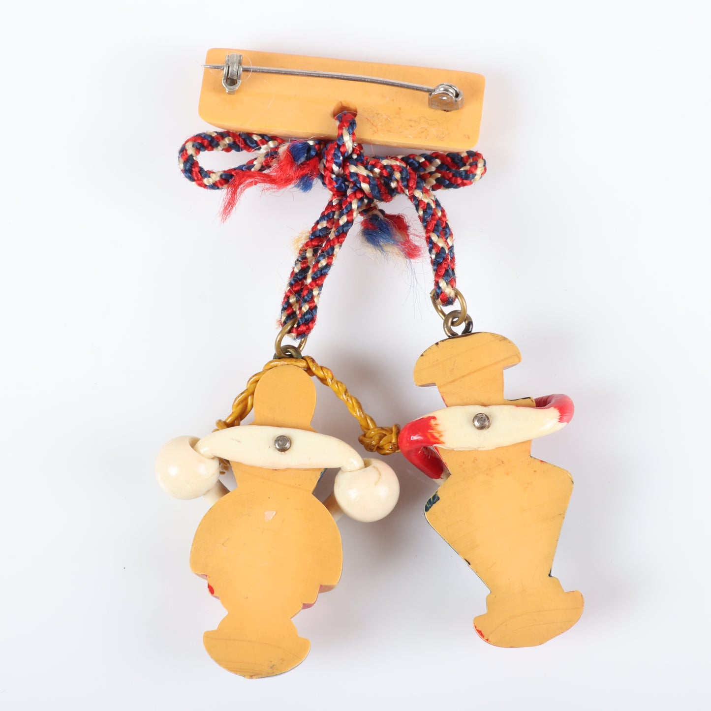 Vintage Bakelite Martha Sleeper bar pin with dangling painted carved German figures. Celluloid arms, waxed string braids, and braided floss bow. Man is missing a plume piece from his cap. 3 1/2" H x 2 1/2" W