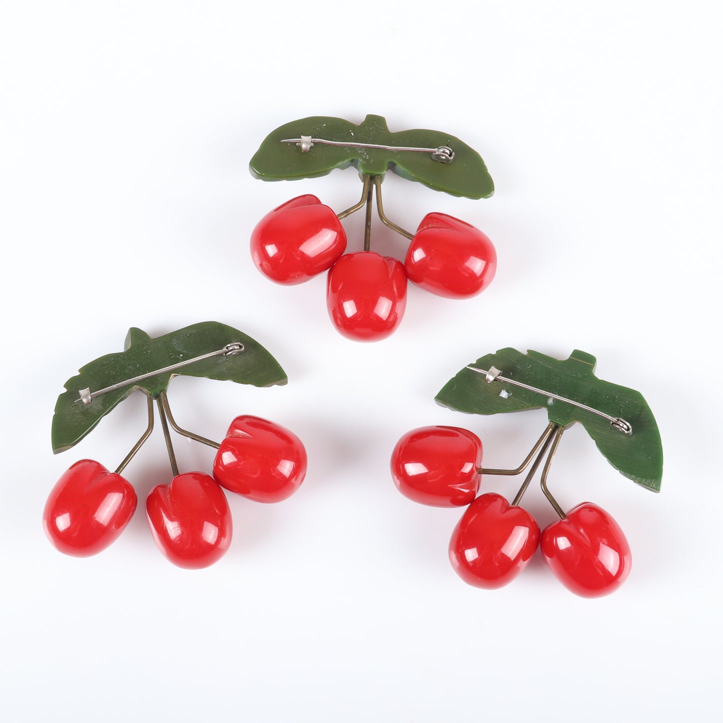 Vintage Bakelite set of 3 unusual cherry fruit pins. Each featuring 3 carved red cherries suspended with metal wire from carved green bakelite leaves. 2 1/4" H x 2 1/2" W