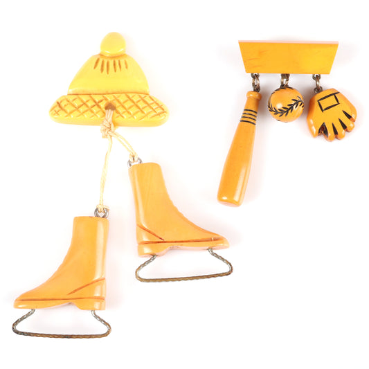 Vintage Bakelite 2pc. sports theme dangle charm pins. Carved butterscotch ice skates and cap, and baseball, bat and glove charms on bar pin. 4 1/4" H x 2 1/2" W (one)