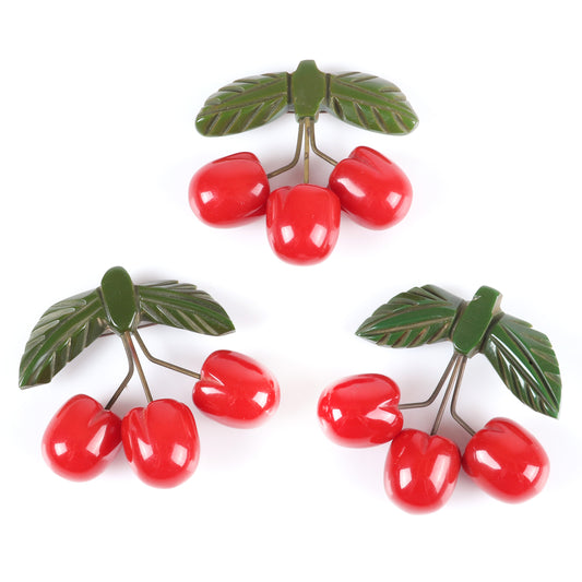 Vintage Bakelite set of 3 unusual cherry fruit pins. Each featuring 3 carved red cherries suspended with metal wire from carved green bakelite leaves. 2 1/4" H x 2 1/2" W